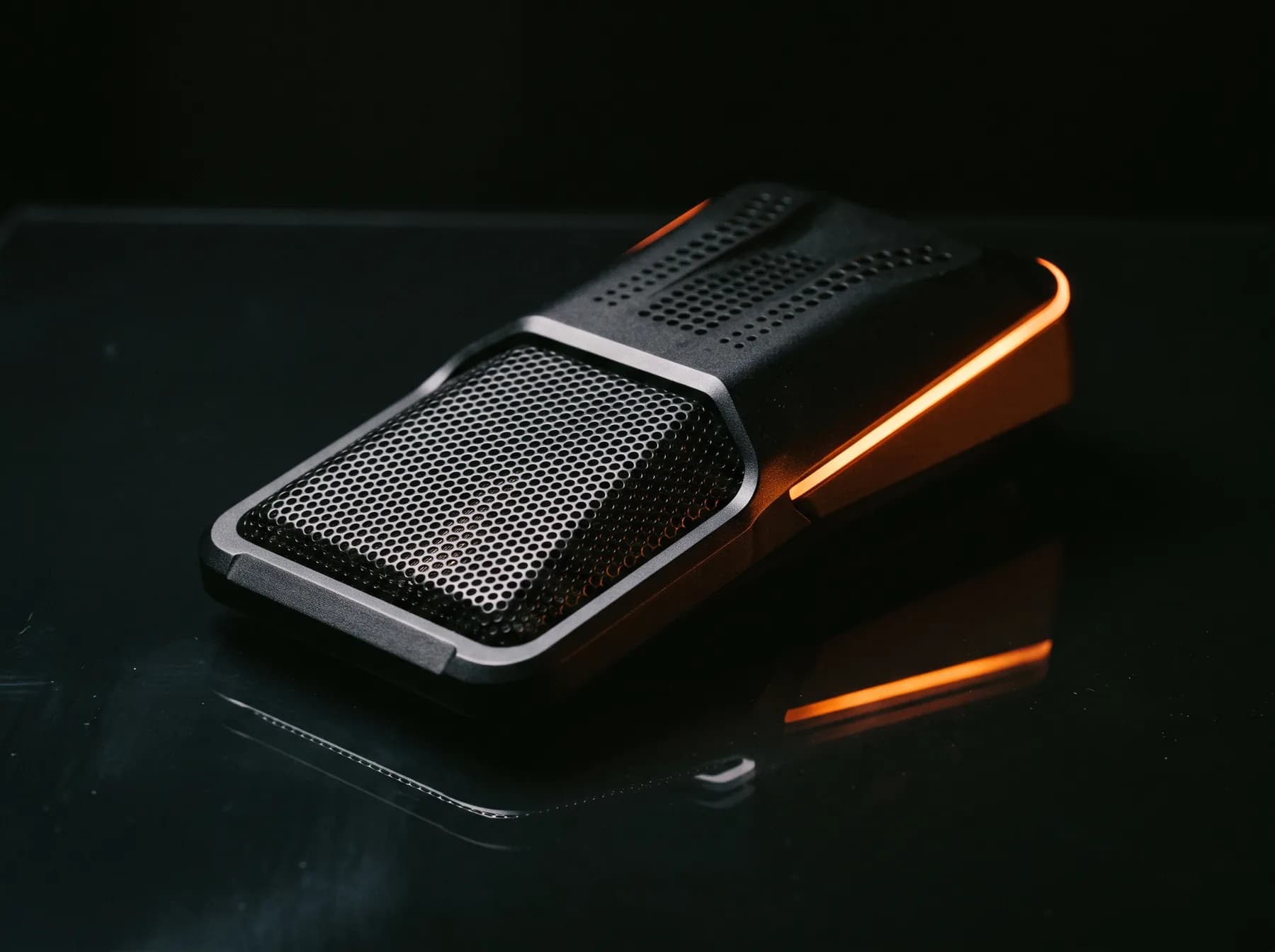 Matte black microphone array module on dark glass under a thin orange rim light