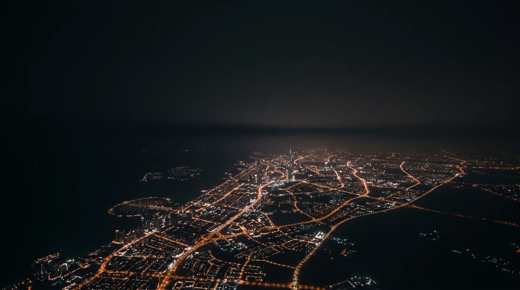 Dubai at night seen from high above, city lights reduced to fine points against a dark sky